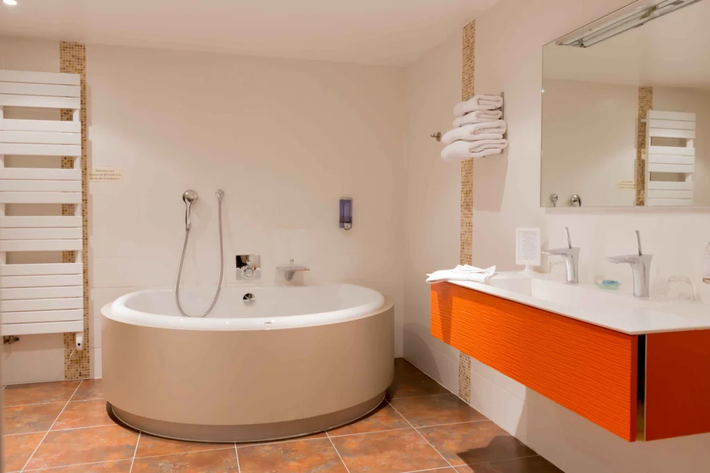 Salle de bain rénovée avec baignoire d’angle et meuble vasque orange